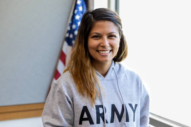 A mid adult female army veteran with a big smile poses in front of the American flag.
